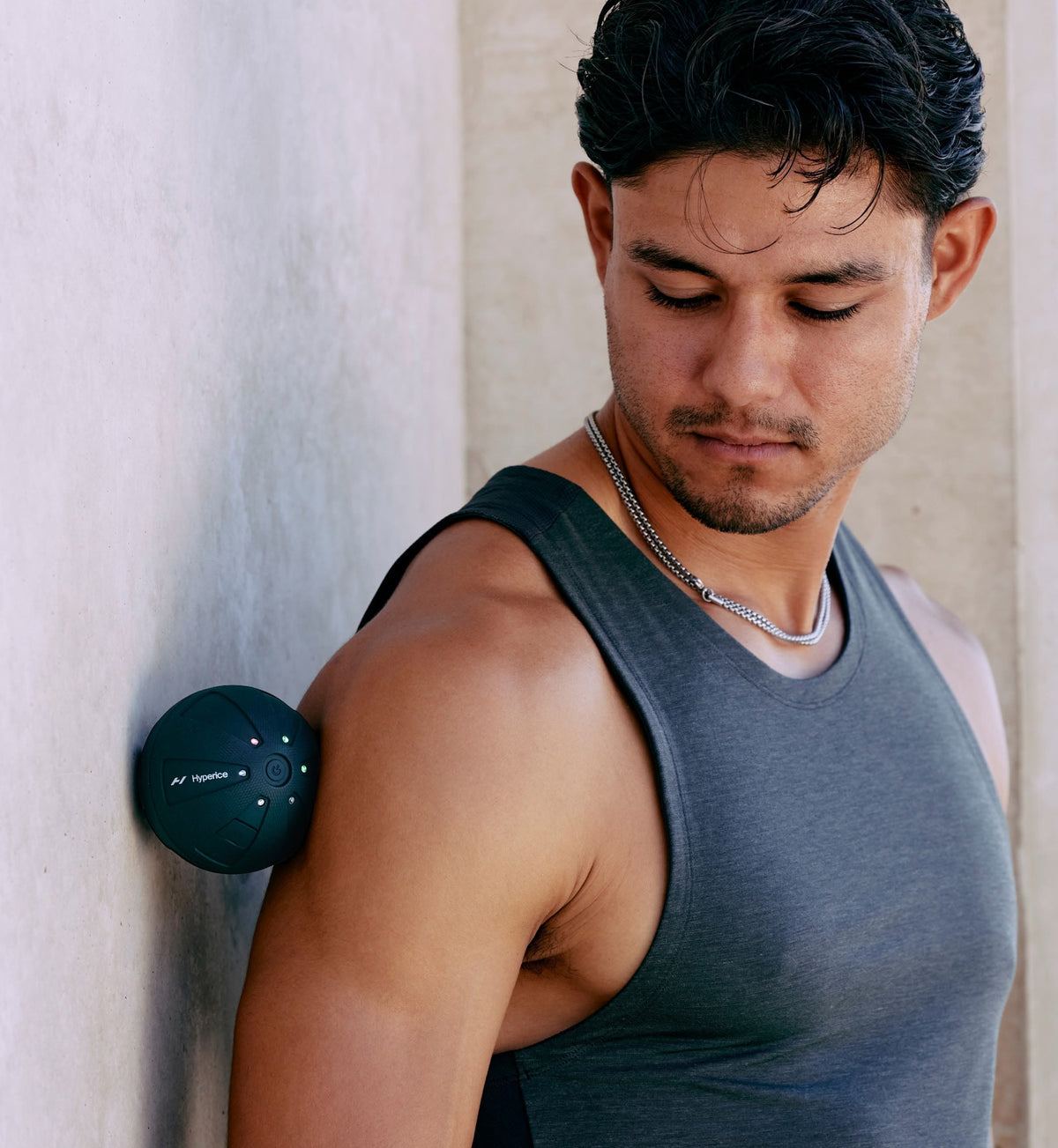 Homme en débardeur gris pressant le Hypersphere Go entre son épaule et un mur clair