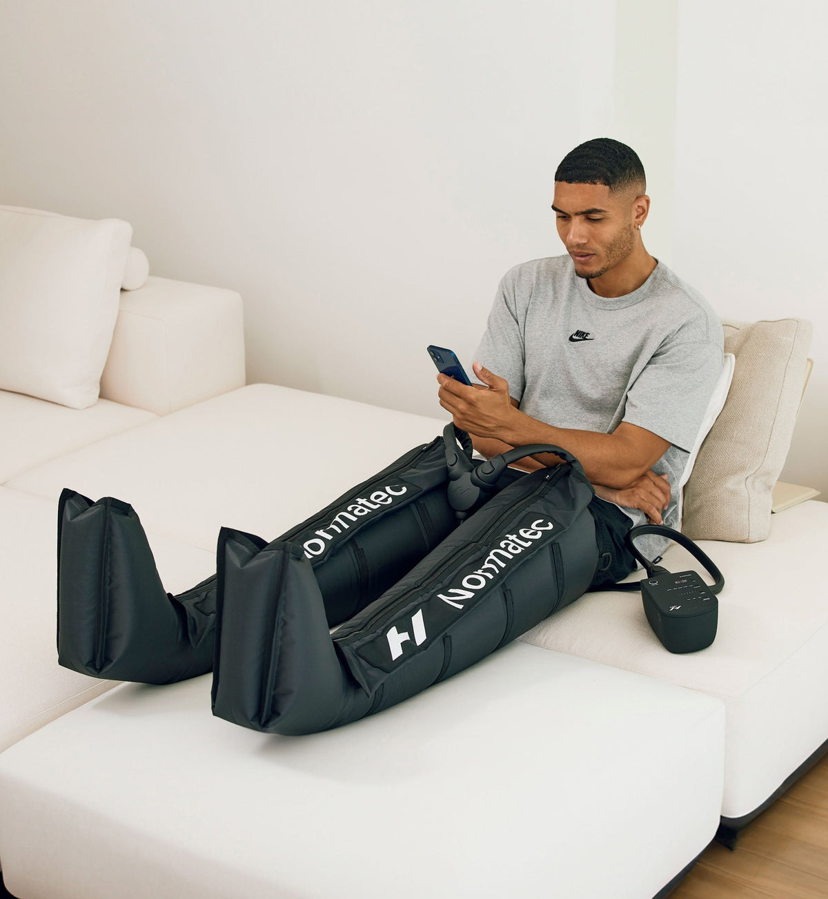 Homme assis sur un canapé, téléphone en main, portant les Normatec 3 Legs aux jambes