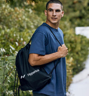 Man holding a black Hyperice bag outdoors with greenery in the background