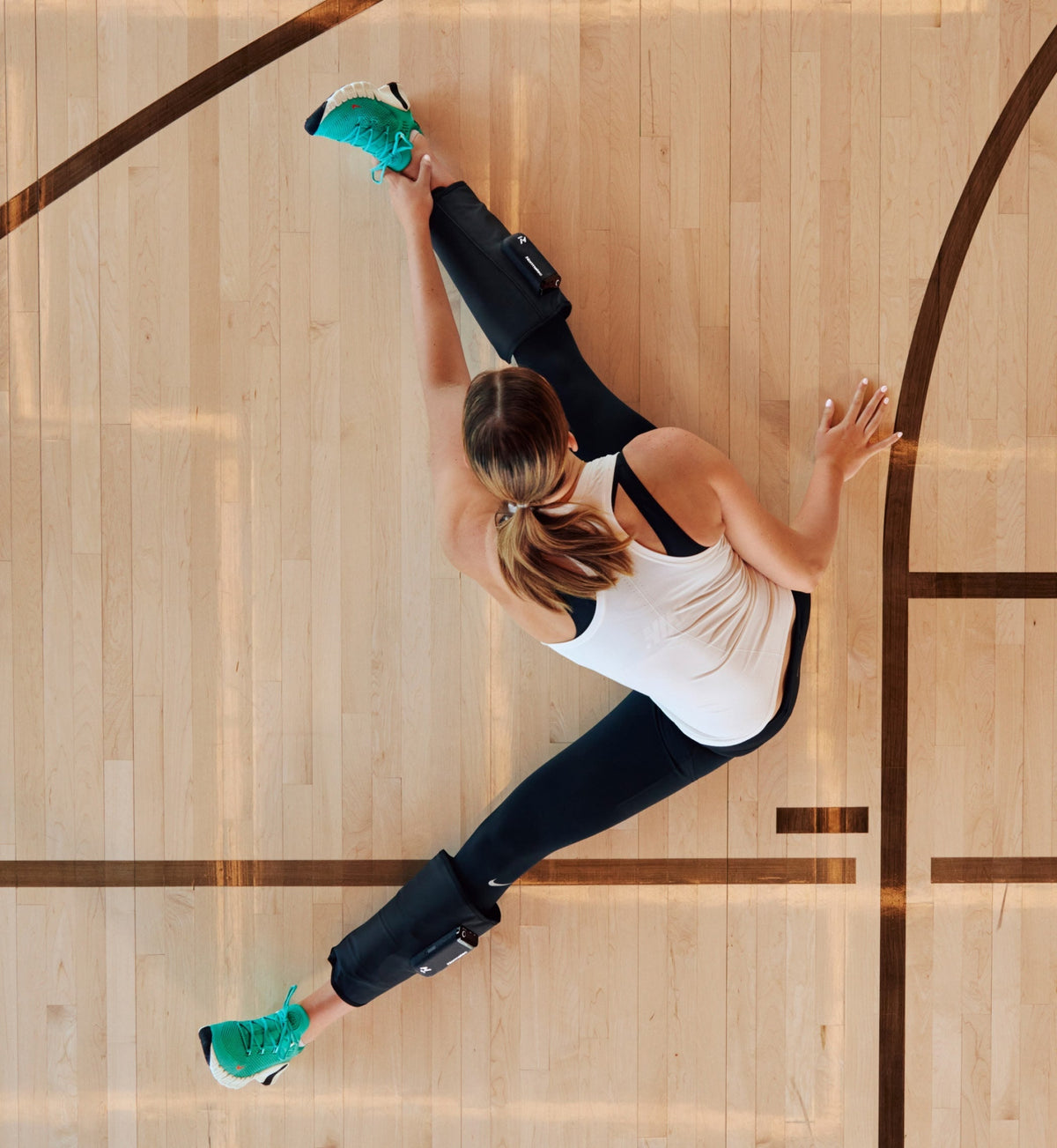 Femme s’étirant sur un terrain de basket avec les Normatec Lower Legs